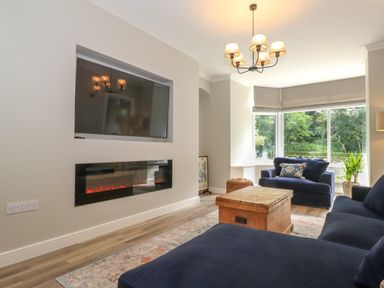 A living room with sofas a wooden chest coffee table wall mounted television and electric fireplace at Eller Cottage in Windermere
