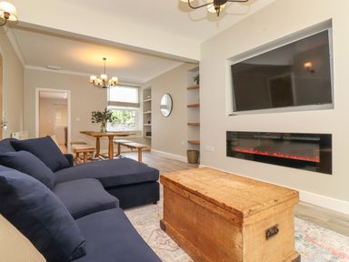 A living room with a navy sofa a wooden chest table a wall-mounted tv and electric fireplace at Eller Cottage in Windermere