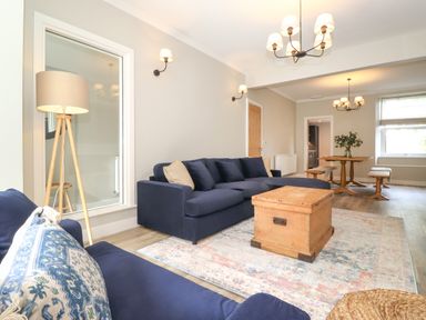 A living room with blue sofas a wooden chest coffee table and dining table at Eller Cottage in Windermere