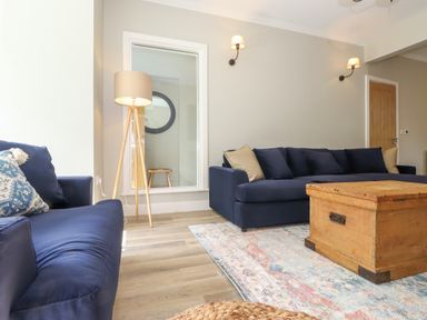 A living room with blue sofas a wooden coffee table a floor lamp and a patterned rug at Eller Cottage in Windermere
