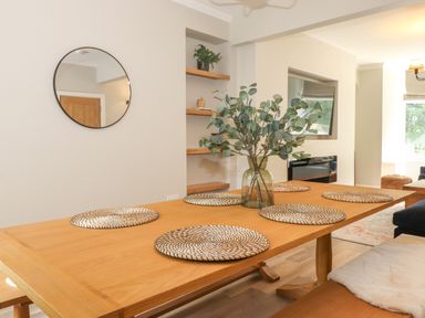A dining room with a wooden table set with round placemats and a vase with green branches at Eller Cottage in Windermere
