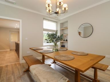A dining room with a wooden table and benches with placemats and a vase with greenery at Eller Cottage in Windermere