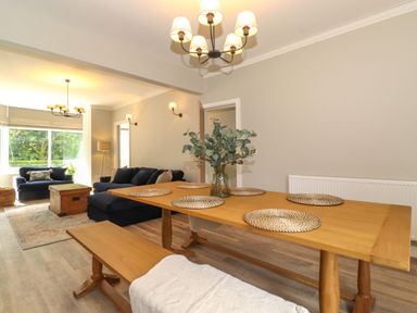 A dining area with a wooden table and benches next to a living room with blue sofas and a wooden chest table at Eller Cottage in Windermere