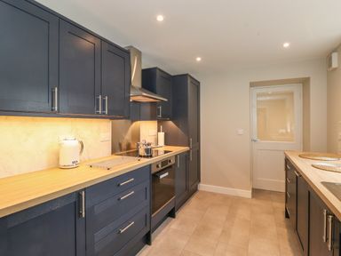 A kitchen with dark cabinets wooden countertops stove kettle and oven at Eller Cottage in Windermere