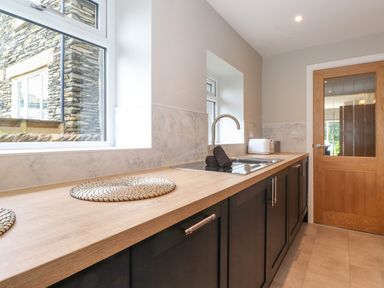 A kitchen with a wooden countertop black cabinets a sink a toaster and woven placemats at Eller Cottage in Windermere