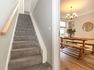 A staircase with grey carpet next to a dining room with wooden benches and a table at Eller Cottage in Windermere