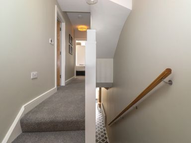 A hallway with carpeted stairs on the left and a wooden handrail on the right at Eller Cottage in Windermere