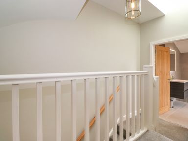 A stair railing with white balusters and a wooden handrail leading to a bathroom with an open wooden door at Eller Cottage in Windermere