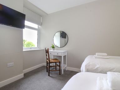 A bedroom with two beds a white desk wooden chair round wall mirror and a wall mounted television at Eller Cottage in Windermere
