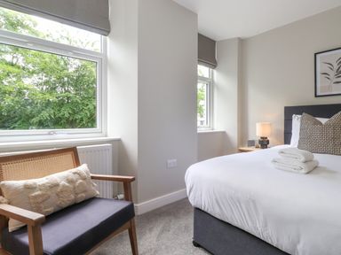 A bedroom with a bed towel set side table lamp an armchair by windows at Eller Cottage in Windermere