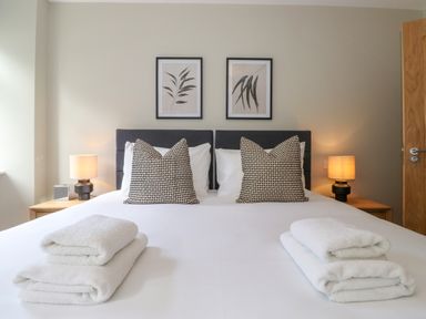 A bedroom with a double bed with two patterned pillows two bedside tables with lamps and folded towels on the bed at Eller Cottage in Windermere