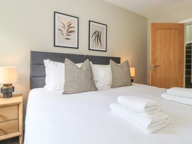 A bedroom with a bed with white linens and patterned pillows beside a wooden nightstand with a lamp at Eller Cottage in Windermere
