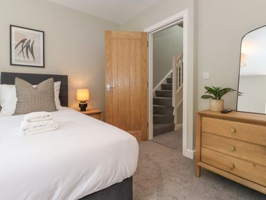 A bedroom with a bed with pillows and towels next to a wooden door and a dresser with a mirror and plant at Eller Cottage in Windermere