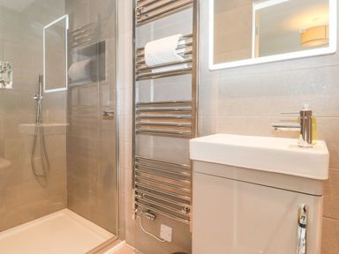 A bathroom with a shower area a towel rack with a towel a sink with a soap dispenser and a backlit mirror at Eller Cottage in Windermere