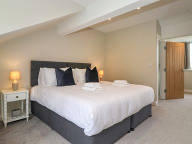 A bedroom with a large bed two bedside tables with lamps and an open wooden door at Eller Cottage in Windermere