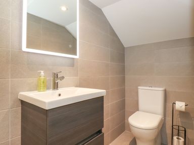 A bathroom with a sink and mirror on the left and a toilet with a toilet paper holder on the right at Eller Cottage in Windermere