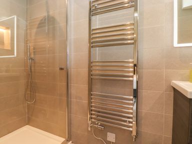 A bathroom with a glass shower enclosure a wall-mounted showerhead and a chrome towel radiator at Eller Cottage in Windermere