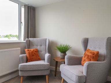Two grey armchairs with orange pillows and a small round wooden table with a plant in a room at Eller Cottage in Windermere