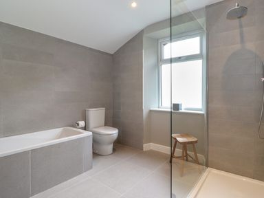 A bathroom with a bathtub toilet shower wooden stool and a window at Eller Cottage in Windermere