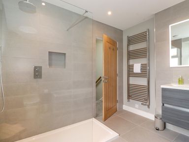 A bathroom with a walk-in shower a wooden door a towel radiator and a sink unit at Eller Cottage in Windermere