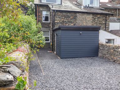 A gravel driveway with a dark blue shed next to a stone house and stone walls at Eller Cottage in Windermere