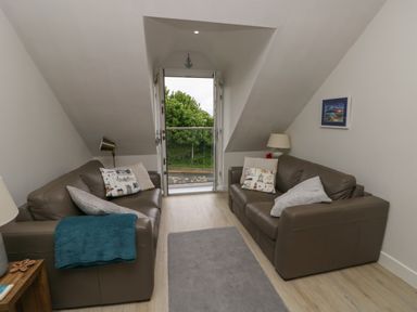 A living room with two leather sofas and a balcony door at Sandy Bay Retreat in Benllech