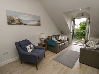 A sitting area with two brown sofas and a blue armchair beside a window opening to a green outdoor view at Sandy Bay Retreat in Benllech