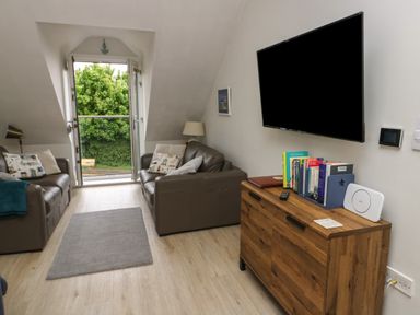 A sitting room with two leather sofas a wooden cabinet with books and a wall mounted television at Sandy Bay Retreat in Benllech