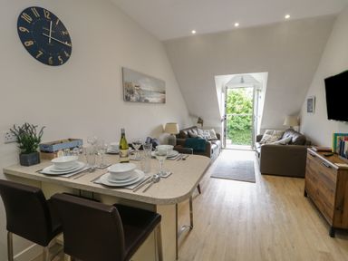 A dining area with a table set for four next to a living room with two sofas and a TV at Sandy Bay Retreat in Benllech