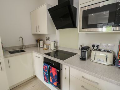 A kitchen with a sink stove oven microwave kettle toaster coffee machine and white cabinets at Sandy Bay Retreat in Benllech