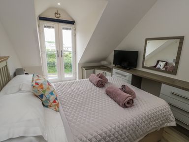 A bedroom with a bed made with towels on top a dresser with a mirror and a television at Sandy Bay Retreat in Benllech