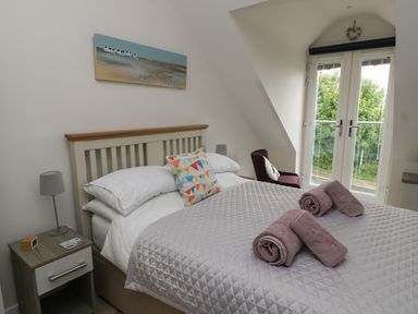 A bedroom with a bed two rolled towels a nightstand lamp an armchair and double doors at Sandy Bay Retreat in Benllech