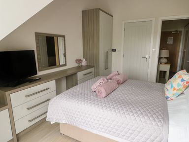 A bedroom with a bed covered with a quilt and towels on it a dresser with a mirror a television and wardrobe at Sandy Bay Retreat in Benllech