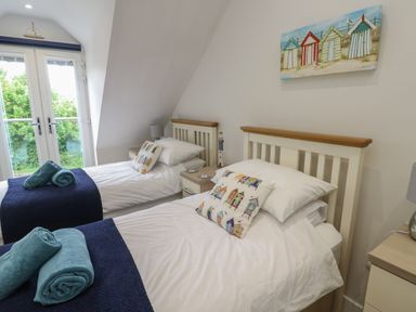 A bedroom with two single beds blue towels on the beds and a painting of beach huts on the wall at Sandy Bay Retreat in Benllech