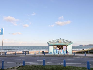 An ice cream kiosk by the seaside with blue bollards and benches near the beach at Sandy Bay Retreat in Benllech