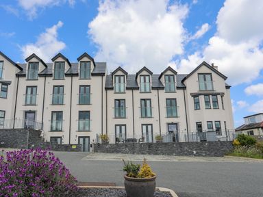 A multi-story residential building with balconies and dormer windows under a blue sky with clouds at Sandy Bay Retreat in Benllech