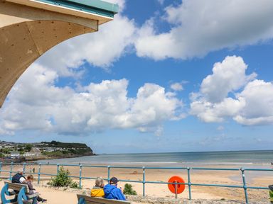 A beach view with people sitting on benches near a railing under a partly covered structure at Sandy Bay Retreat in Benllech