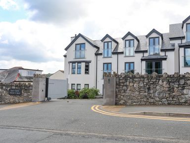A gated residential building with stone walls and multiple windows at Sandy Bay Retreat in Benllech