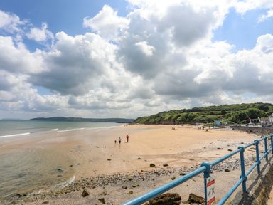 A sandy beach with people walking near the water and a blue railing in the foreground at Sandy Bay Retreat in Benllech