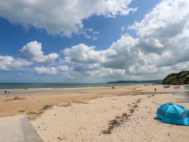 A sandy beach with people walking and a blue tent near the shore at Sandy Bay Retreat in Benllech