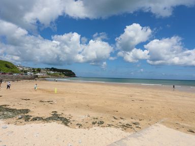 A sandy beach with people playing and walking near the ocean under a partly cloudy sky