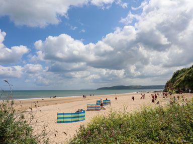 A sandy beach with people and colorful windbreaks under a cloudy sky at Sandy Bay Retreat in Benllech