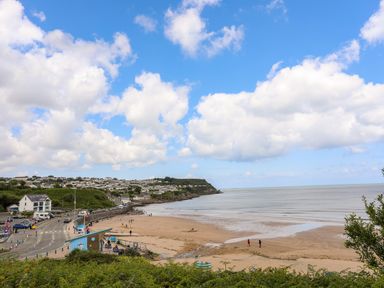 A sandy beach with people walking near the shoreline and houses on a hill by the sea at Sandy Bay Retreat in Benllech