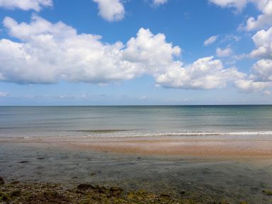 A beach with pebbles and sand meeting a calm sea under a blue sky with clouds at Sandy Bay Retreat in Benllech