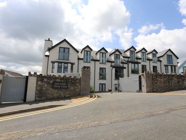 A multi story residential building with multiple windows and balconies behind a stone wall with a gate at Bay View Trem Y Bae in Benllech