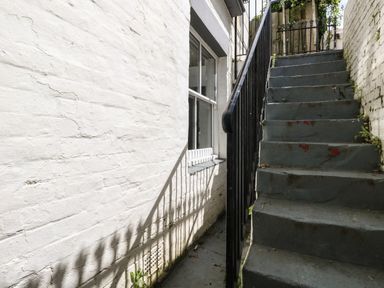 A narrow outdoor stairway with black metal railing next to a white brick wall and window at Flat 1 - Sandbanks in Bournemouth