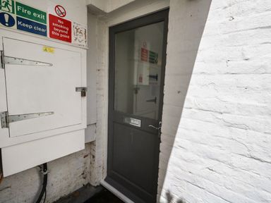A gray door with a mail slot and number 1 next to a white utility box with fire exit and no smoking signs on a white brick wall at Flat 1 - Sandbanks in Bournemouth