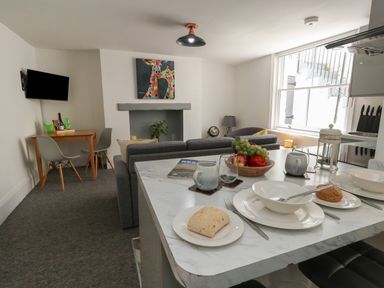 A kitchen and living area with a table set with plates and a bowl of fruit at Flat 1 - Sandbanks in Bournemouth