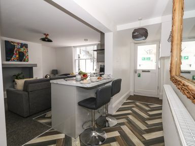 A kitchen and living room area with a breakfast bar with stools and a door at Flat 1 - Sandbanks in Bournemouth