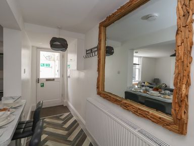 A narrow hallway with a door at the end and a wooden framed mirror on the wall reflecting a dining table with chairs at Flat 1 - Sandbanks in Bournemouth